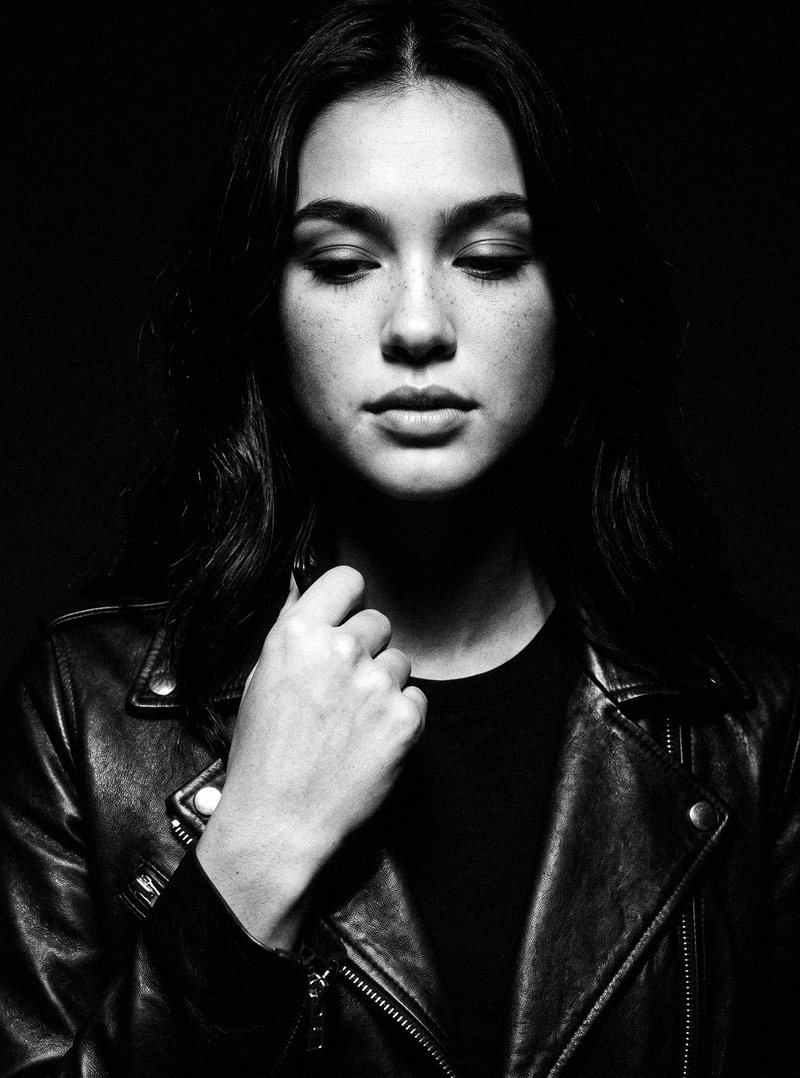 Nova Rai holding the collar of her leather jacket, eyes down, in black and white