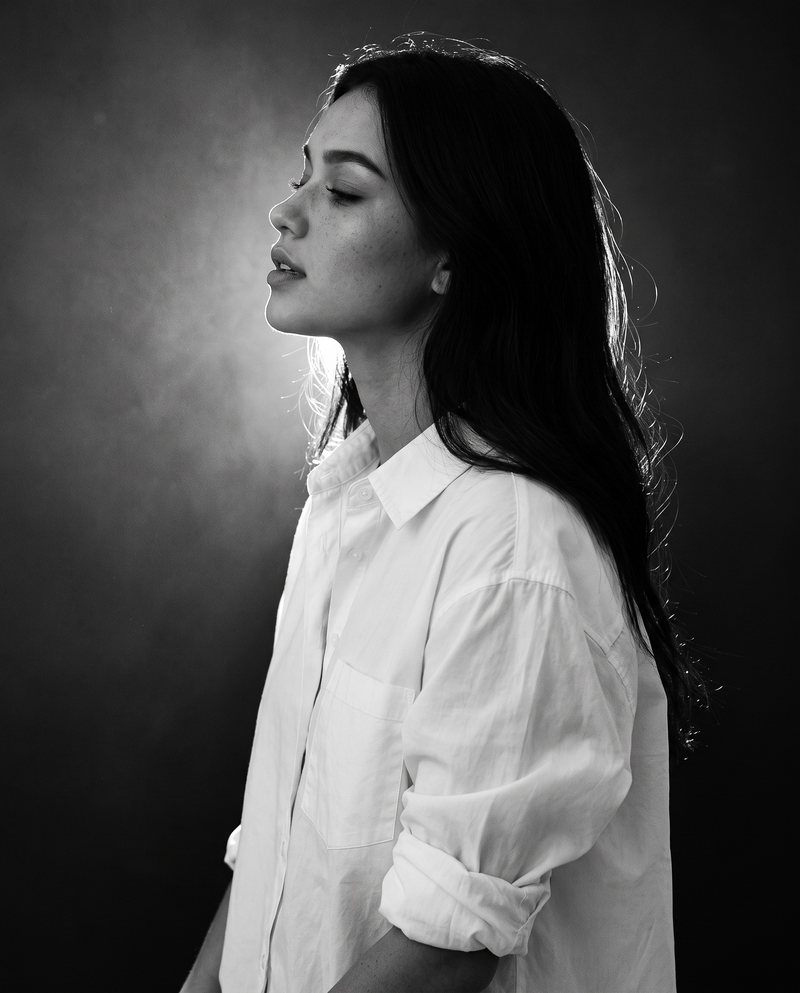 Nova Rai in profile with her eyes closed against a soft backlight, in black and white