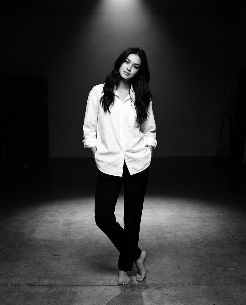 Nova Rai standing barefoot under a spotlight with her hands in her pockets, in black and white