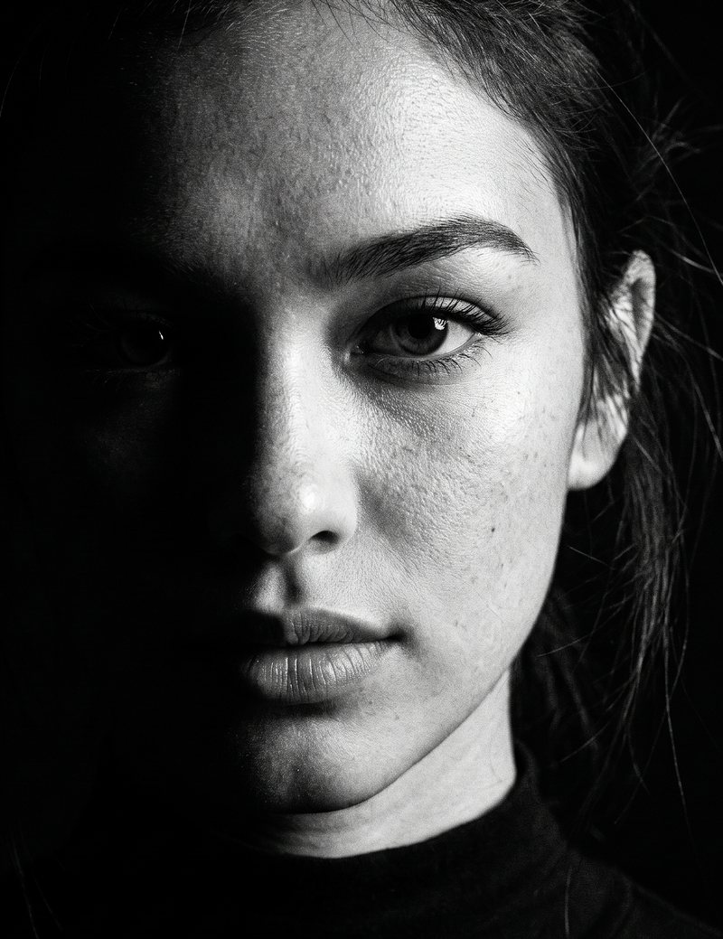 Nova Rai with half her face in shadow and one eye in the light, in black and white
