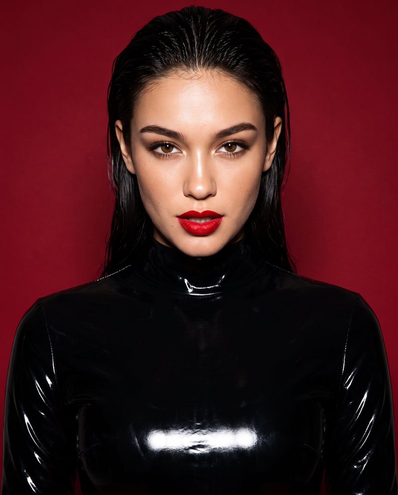 Nova Rai with her hair slicked back and red lips against a red wall