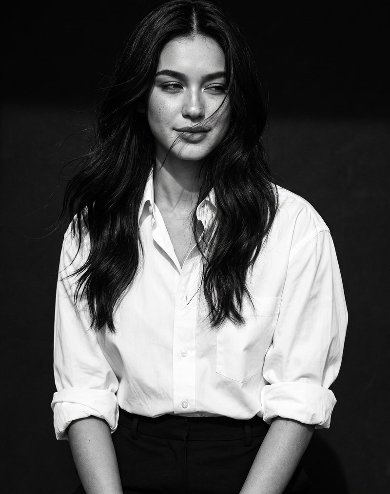 Nova Rai in a white shirt with a faint smile, looking away, in black and white